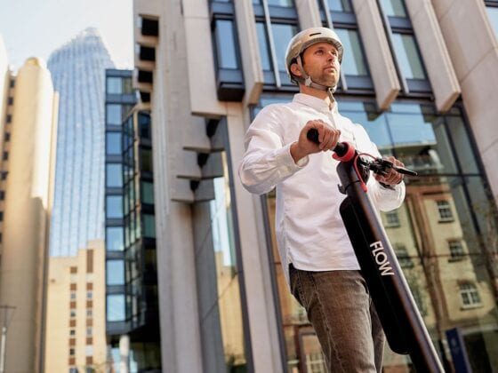 Man riding St-Kilda Flow electric scooter in city wearing Bern helmet